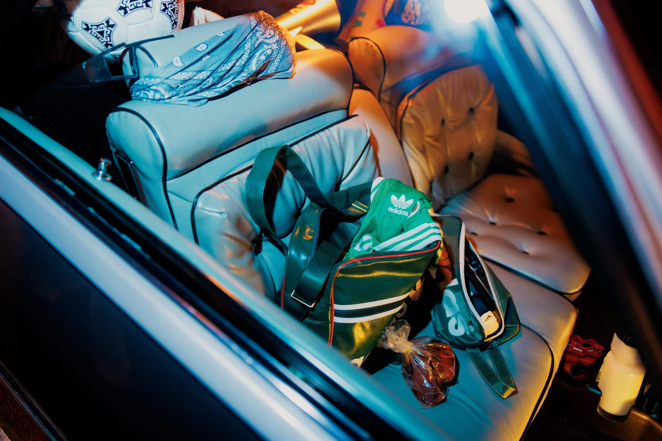 Shot through a car window at night. A green adidas holdall and a football on the back seat, neon streaking across the glass
