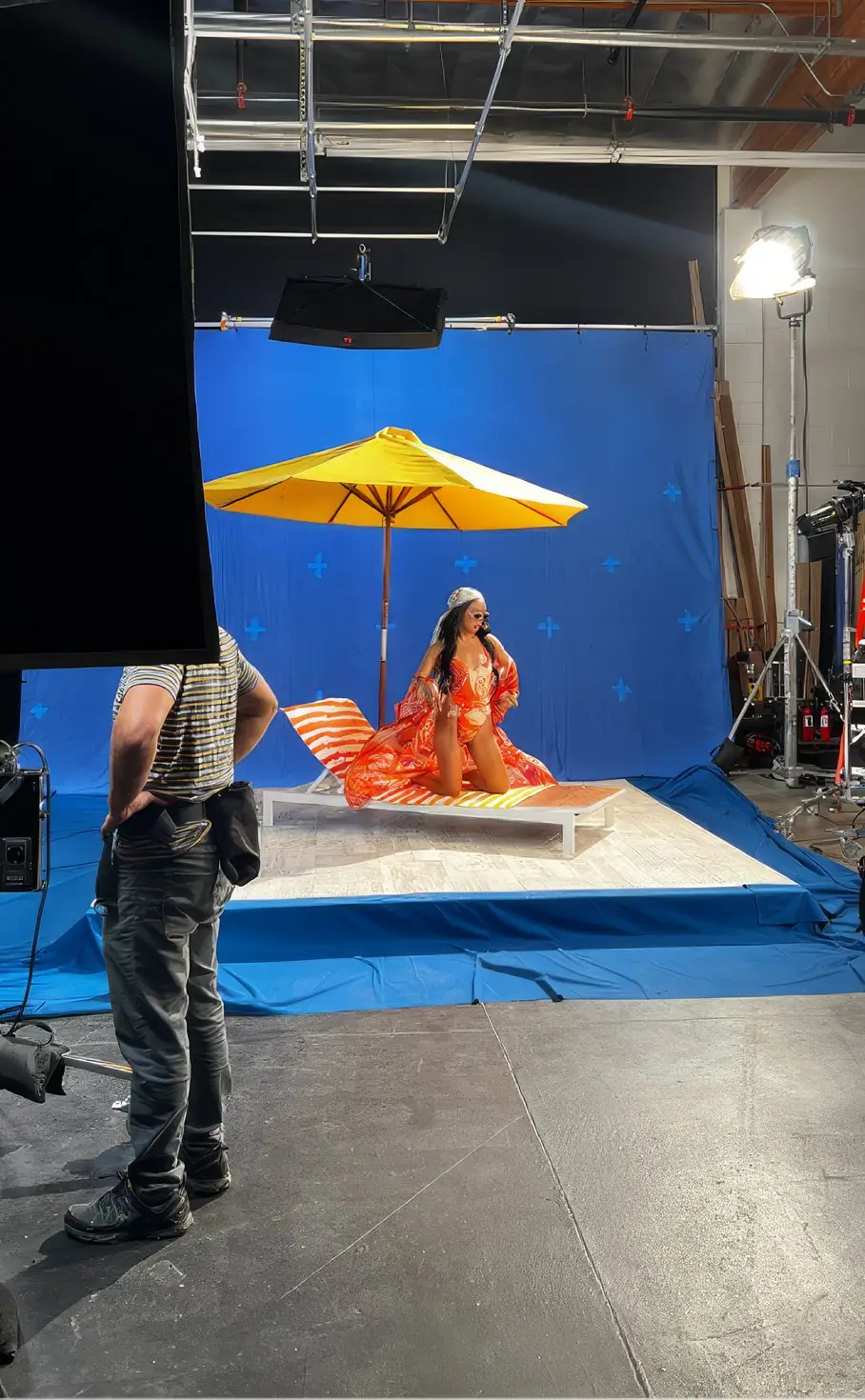 A GUESS shoot in progress on a studio stage. Cyclorama, parasol, grip stands, and a crew member watching from the foreground