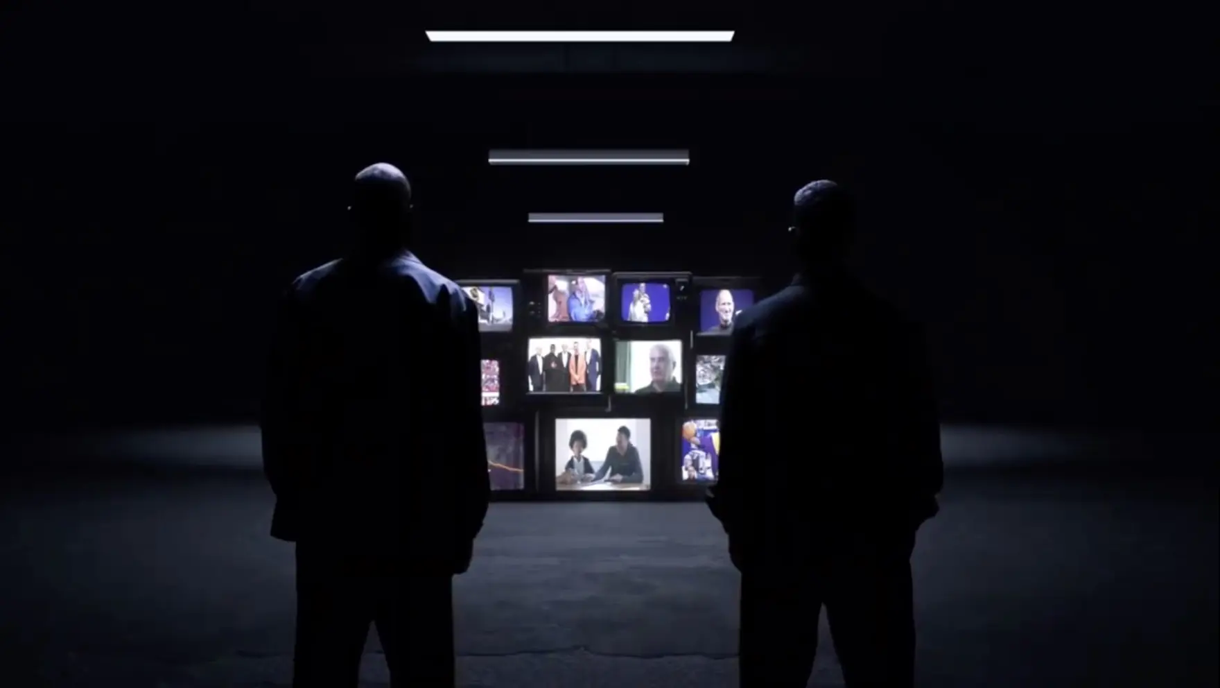 Two people standing in a dark room in front of a wall of monitors, watching the cut play back